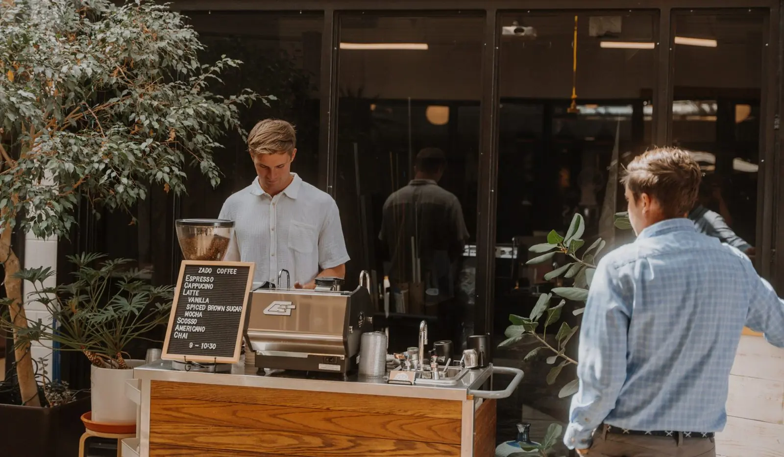 A Zado barista pulling a shot at the wooden cart, letterboard menu in front, as a guest walks up