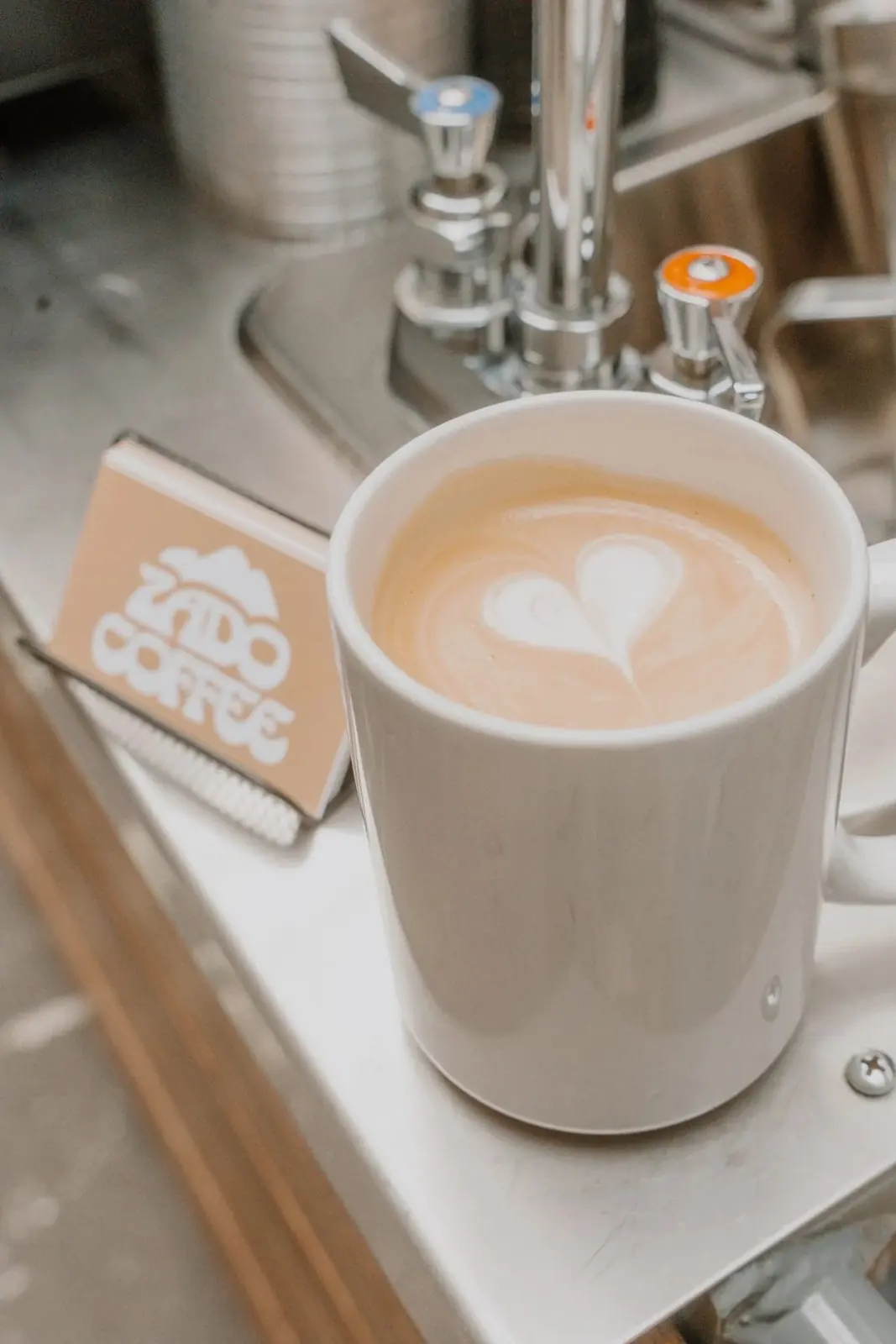 A latte with a heart poured on top, next to a Zado Coffee coaster