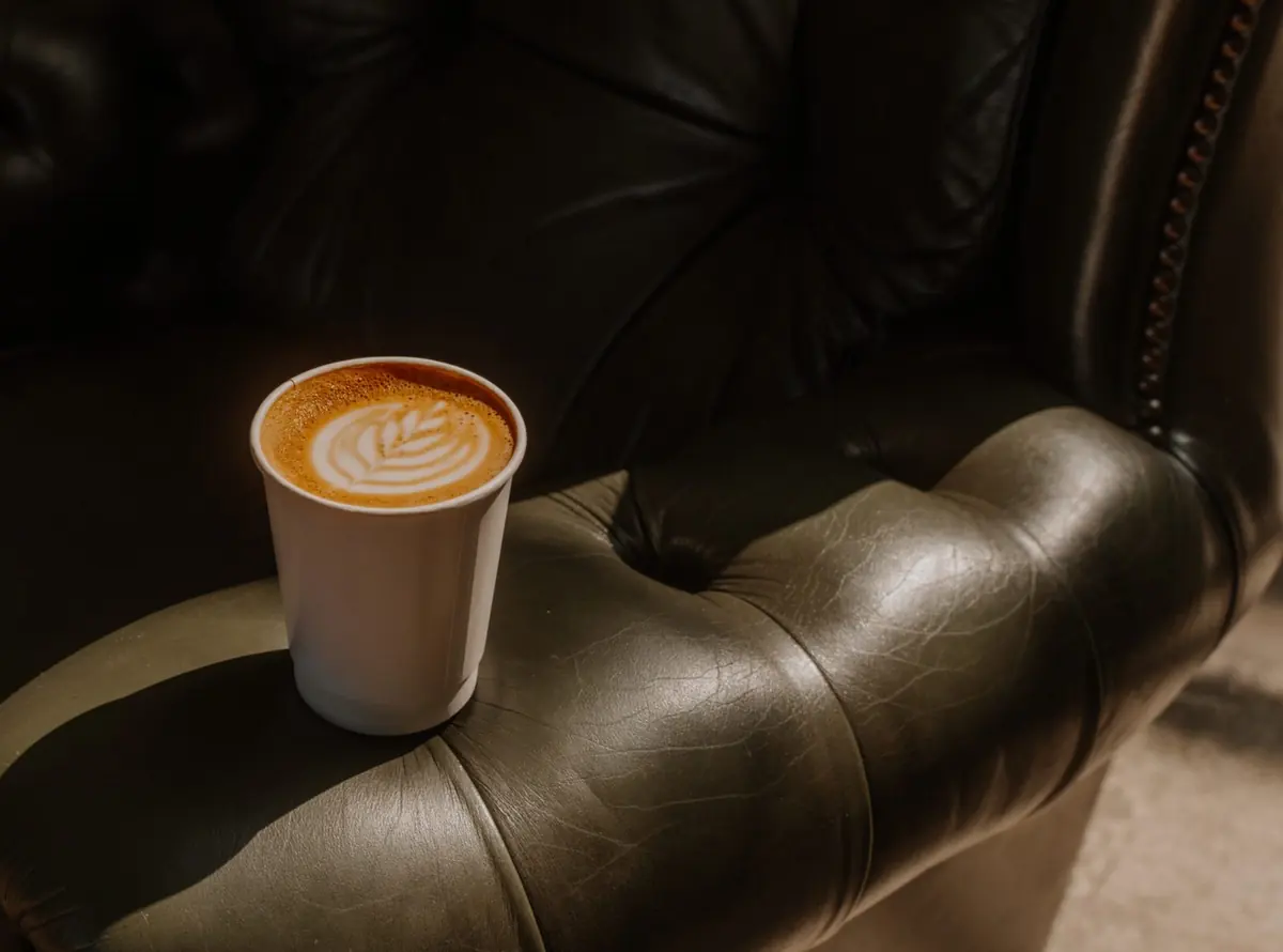 A latte with rosetta art resting on the arm of a leather couch