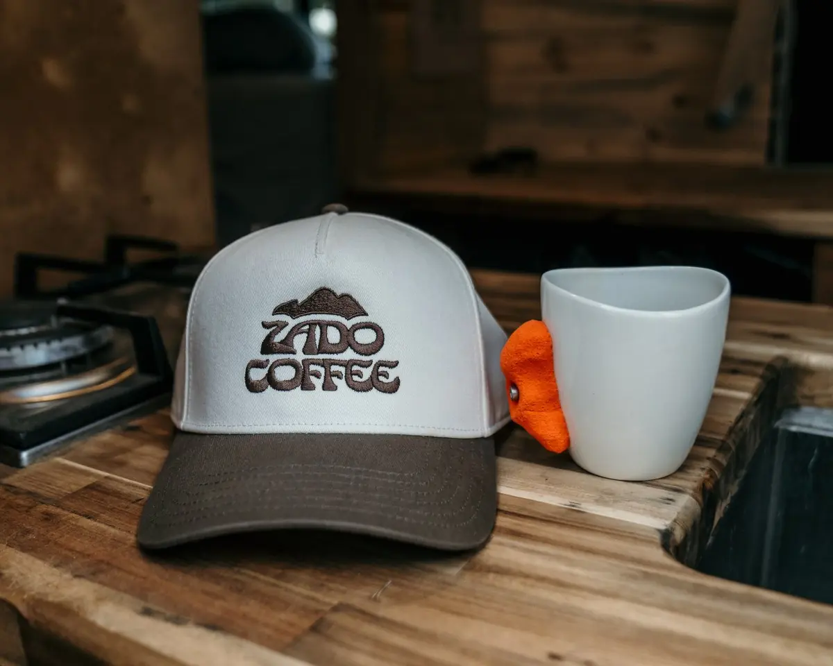 The Zado Two-Tone Hat next to a mug on a wood counter