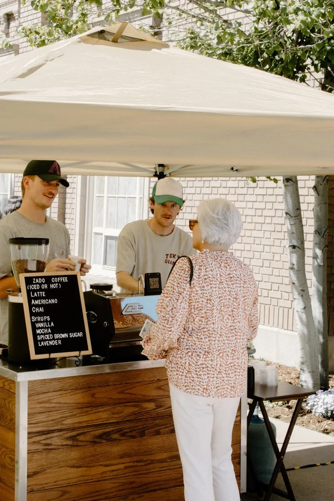 Two Zado baristas under a tent serving a guest