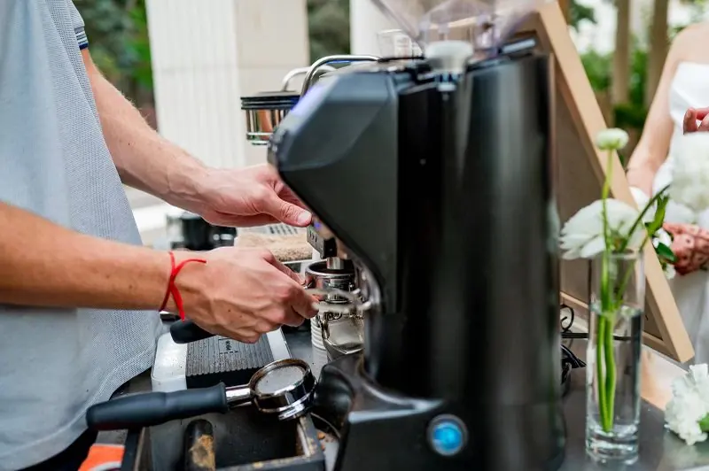 A barista at the grinder with wedding flowers nearby